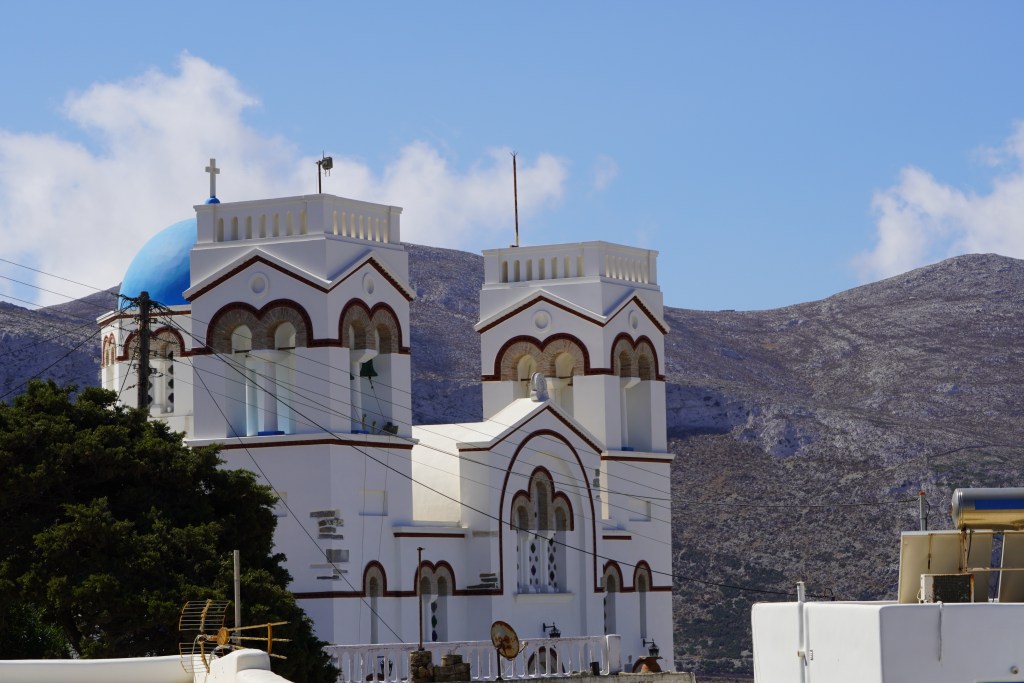Church in Tholaria with blue, red and white colors. Mountains in background.