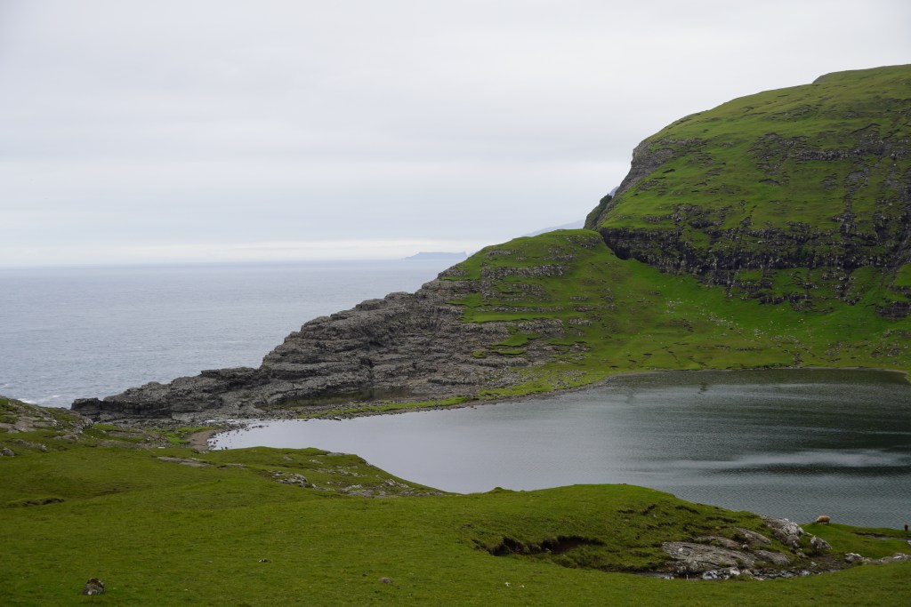 Leitisvatn (largest lake of the country) with the Atlantic Ocean in the background. Lush green mountain and meadows.